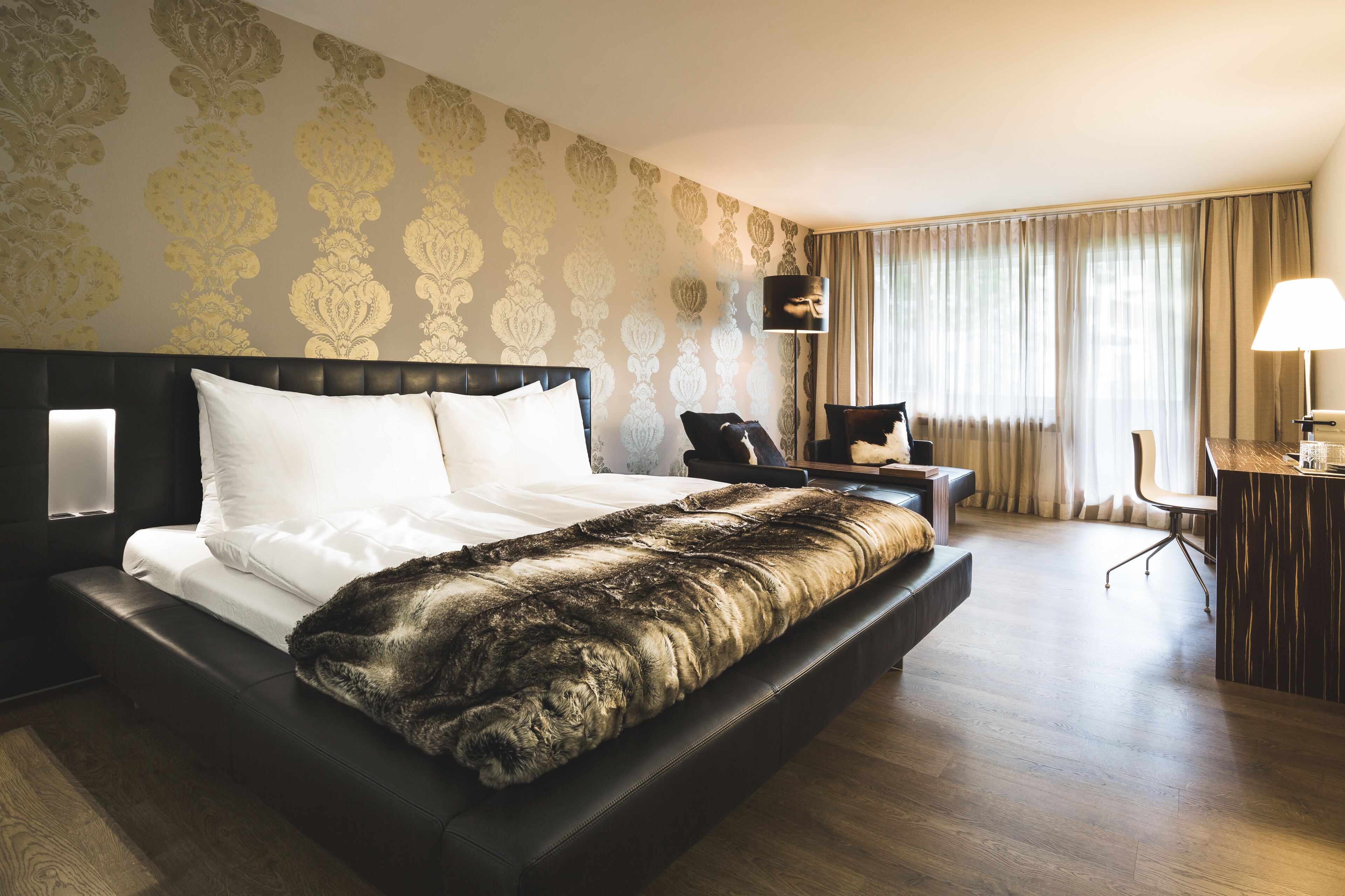 A hotel room with a large bed, a desk with a chair, and a lamp.