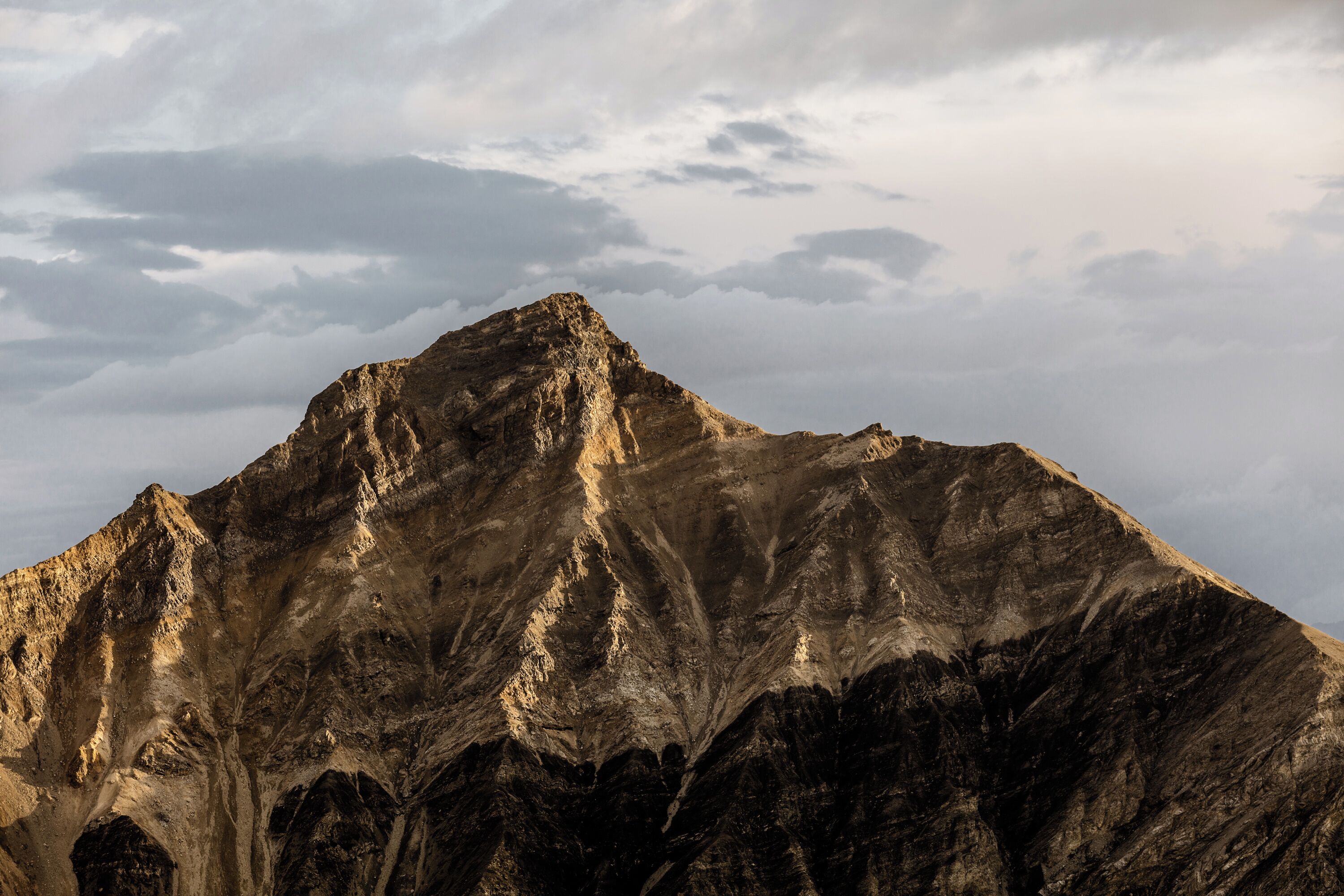 A mountain with rugged terrain and a cloudy sky.