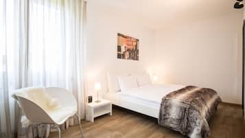 Ein Schlafzimmer mit einem Bett, einem weißen Stuhl, einem Nachttisch, einer Lampe und einem Poster an der Wand.
