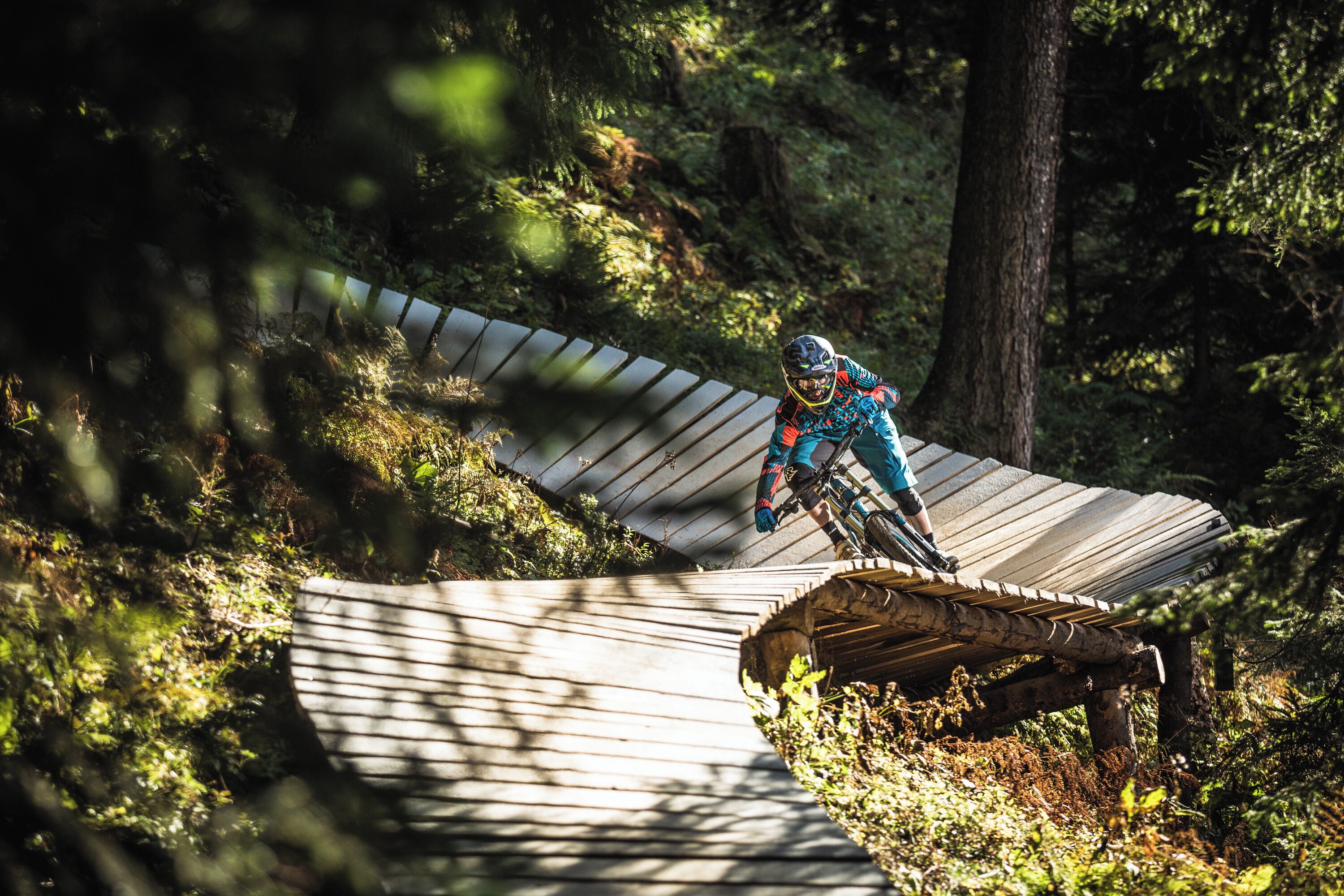 Uma pessoa anda de bicicleta de montanha numa trilha de madeira em uma área arborizada.