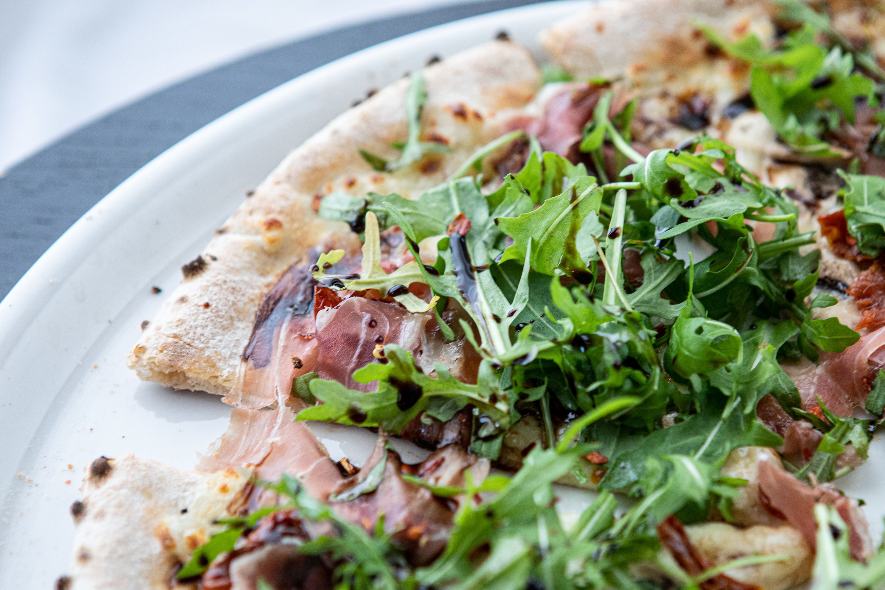 A pizza with arugula and prosciutto on a white plate.