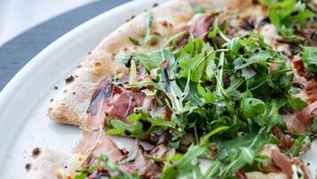 A pizza with arugula and prosciutto on a white plate.