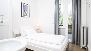 Una habitación de hotel moderna con una cama, una mesita de noche con lámpara, una ventana con cortinas y vistas al exterior.