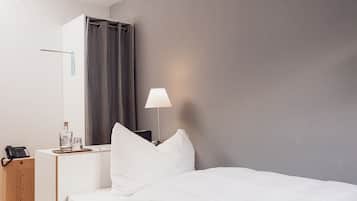 Una camera d'albergo con un letto, un comodino con una lampada, un telefono e un minibar.