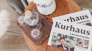 Une table en bois sur laquelle se trouvent une bouteille d’eau, deux verres et un magazine intitulé « Kurhaus Lenzerheide ».