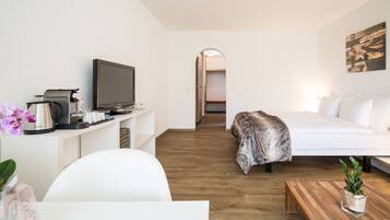 Una habitación de hotel moderna con una cama, un televisor, una cafetera y una mesita con una planta.