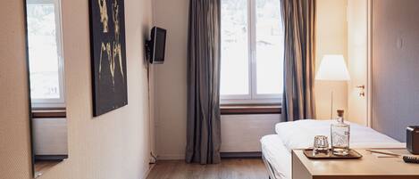 Habitación de hotel con cama, mesita de noche, lámpara y ventana con cortinas.
