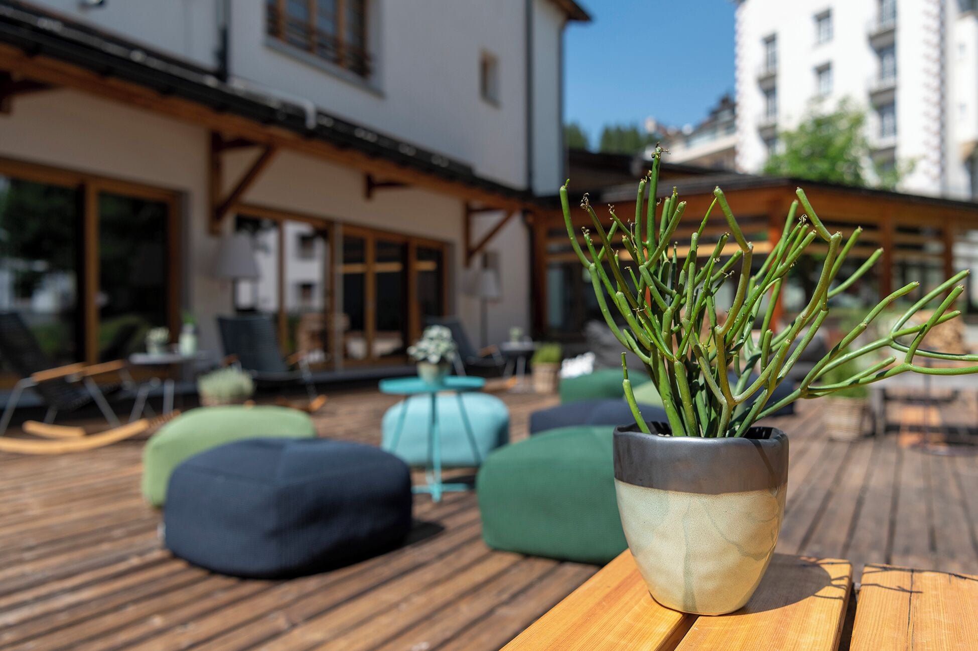 Une terrasse en bois avec un pot de fleurs, des sièges d’extérieur et un bâtiment en arrière-plan.