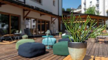 Une terrasse en bois avec un pot de fleurs, des sièges d’extérieur et un bâtiment en arrière-plan.