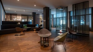 A modern interior with a wooden floor, a dining area with chairs, a sofa, and a large window with curtains.