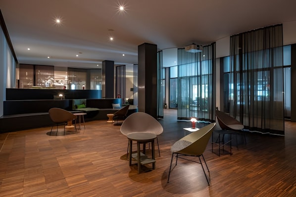 A modern interior with a wooden floor, a dining area with chairs, a sofa, and a large window with curtains. - Schweizerhof (Vaz-Obervaz)
