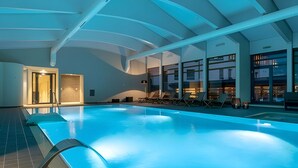 An indoor swimming pool with clear water, surrounded by lounge chairs and a modern architectural design.