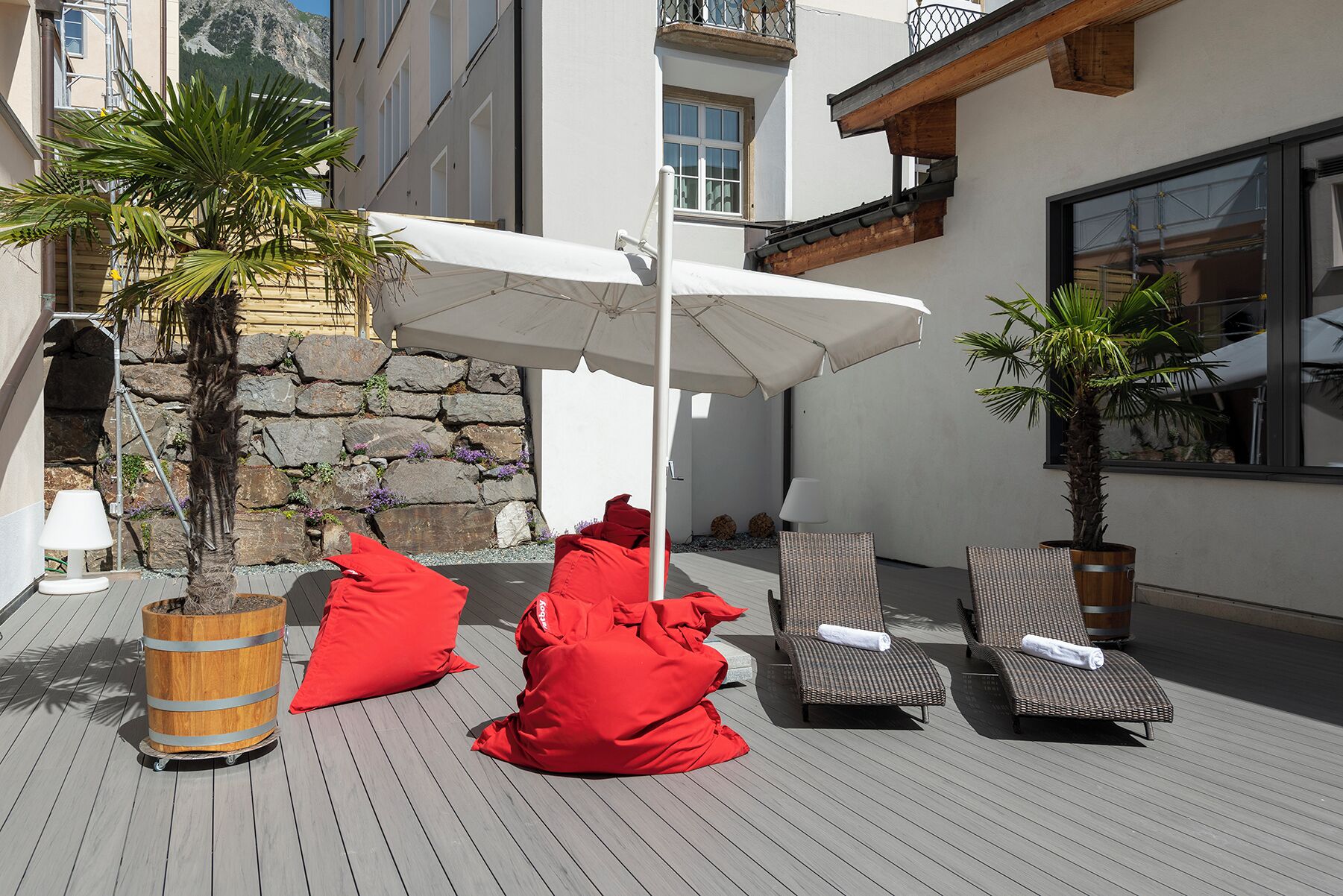 Eine Terrasse mit Liegestühlen, einem weißen Sonnenschirm und einer Steinmauer.