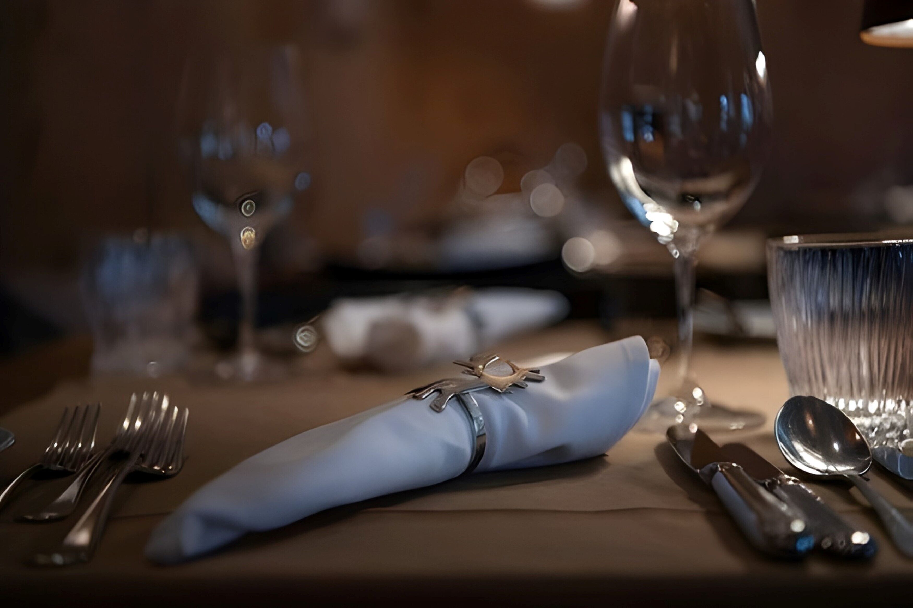 Une table dressée avec une serviette pliée, des couverts et un verre.