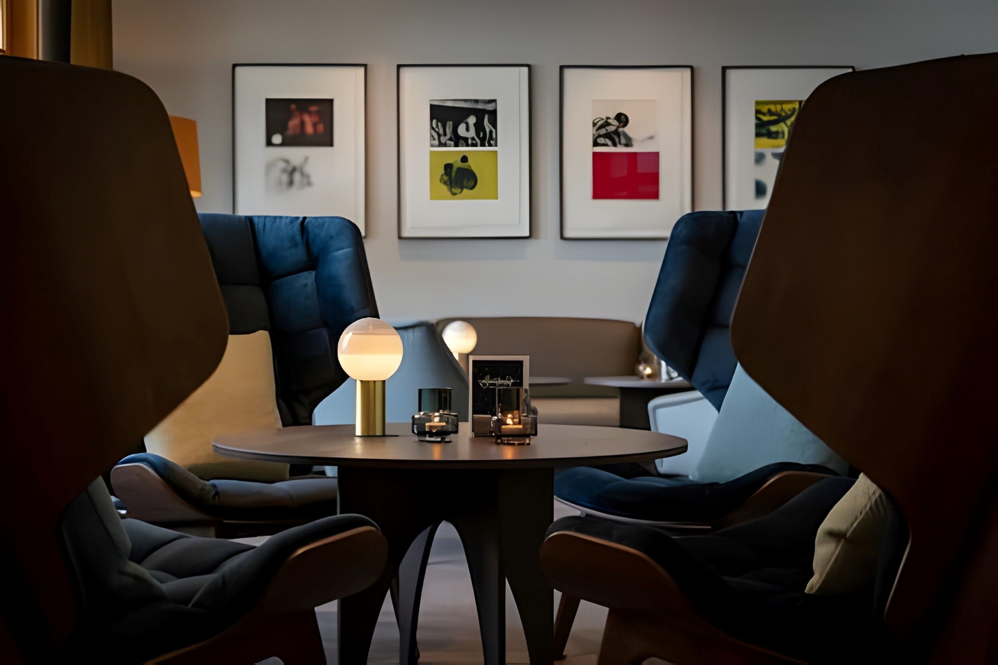 Un área de estar moderna con una mesa redonda, dos sillones azules y una lámpara.