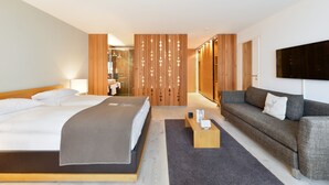 A modern hotel room with a large bed, a sofa, a coffee table, and a TV mounted on the wall.