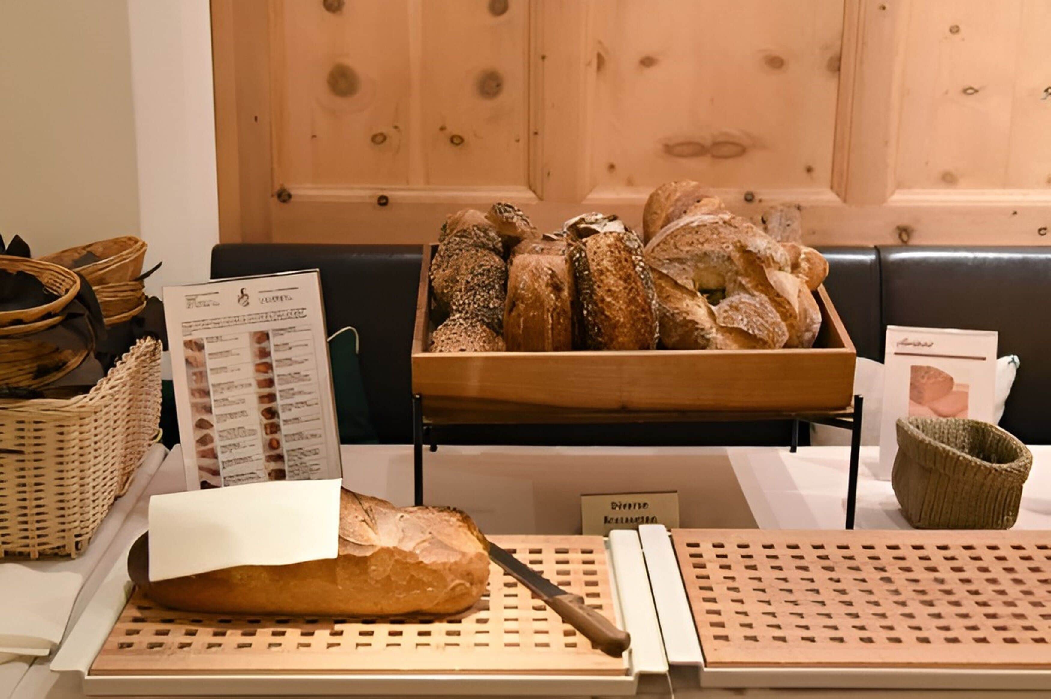 A display of various breads on a wooden table with a knife, baskets, and a menu sign.
