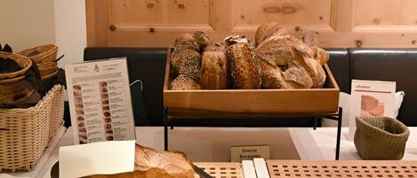 A display of various breads on a wooden table with a knife, baskets, and a menu sign.