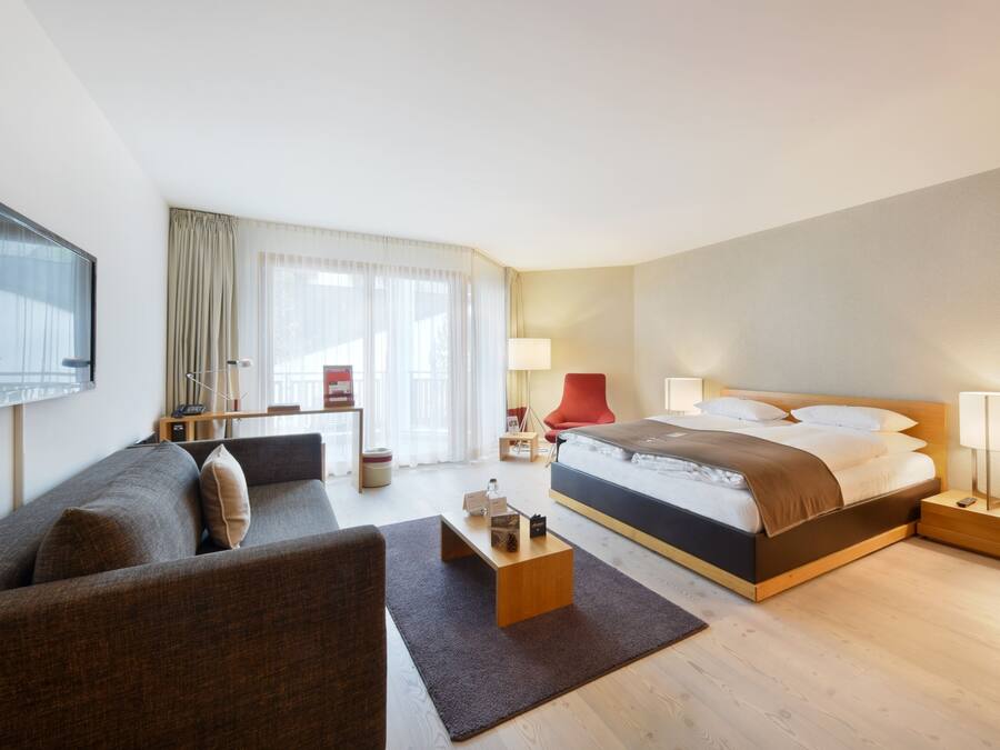 Hotellihuone, jossa on sänky, sohva, televisio, työpöytä ja lamppu.
