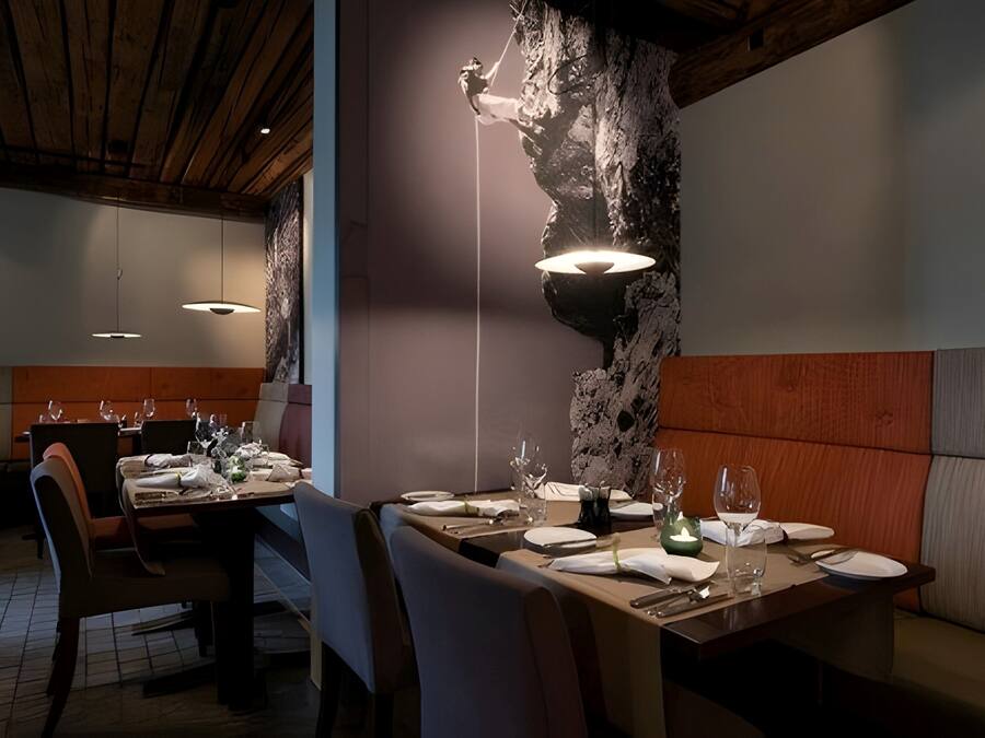 A restaurant with wooden ceiling beams, a stone wall with a climbing figure, and tables set for dining.