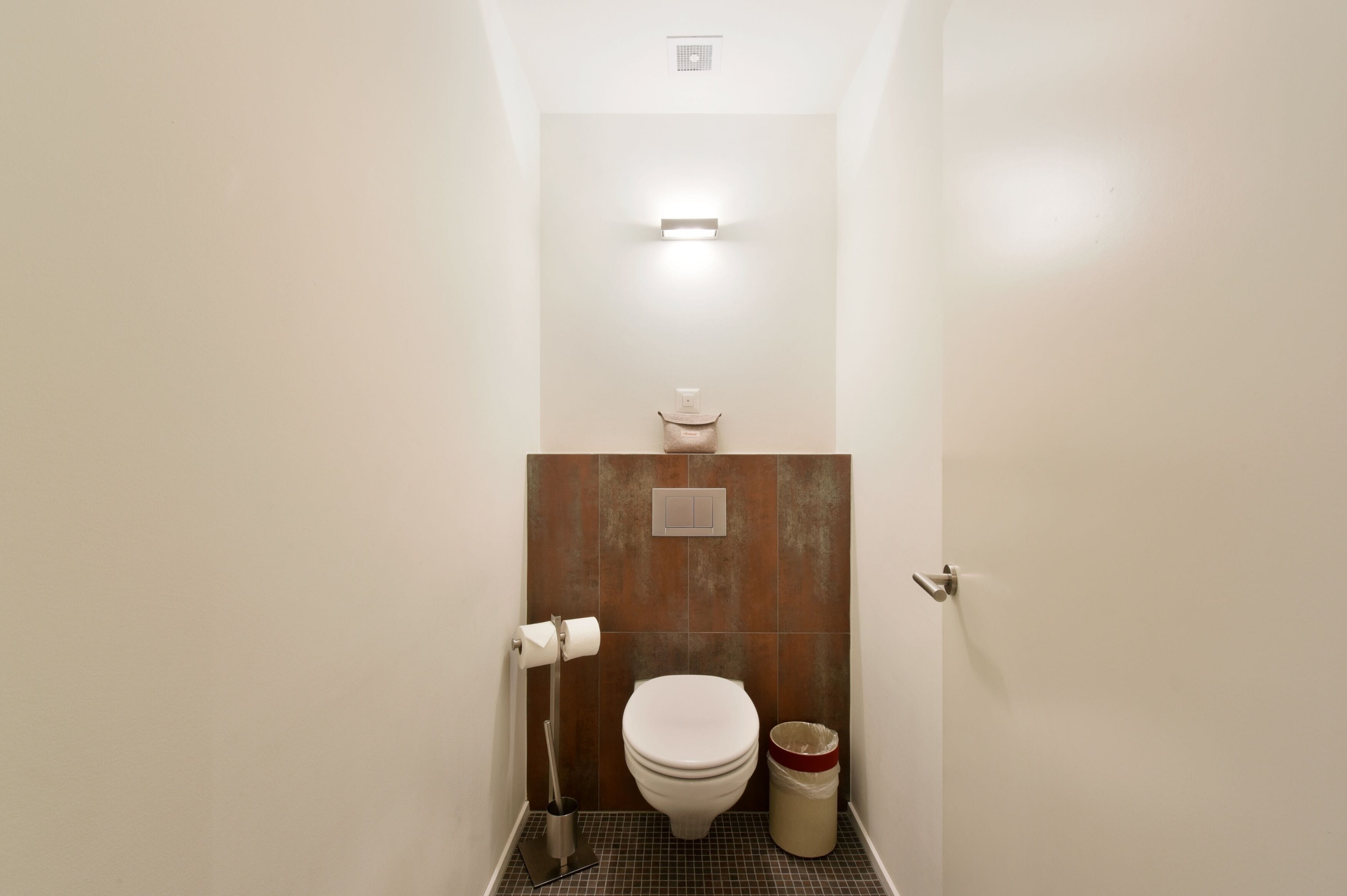 A small, modern bathroom with a toilet, a trash can, and a toilet paper holder.
