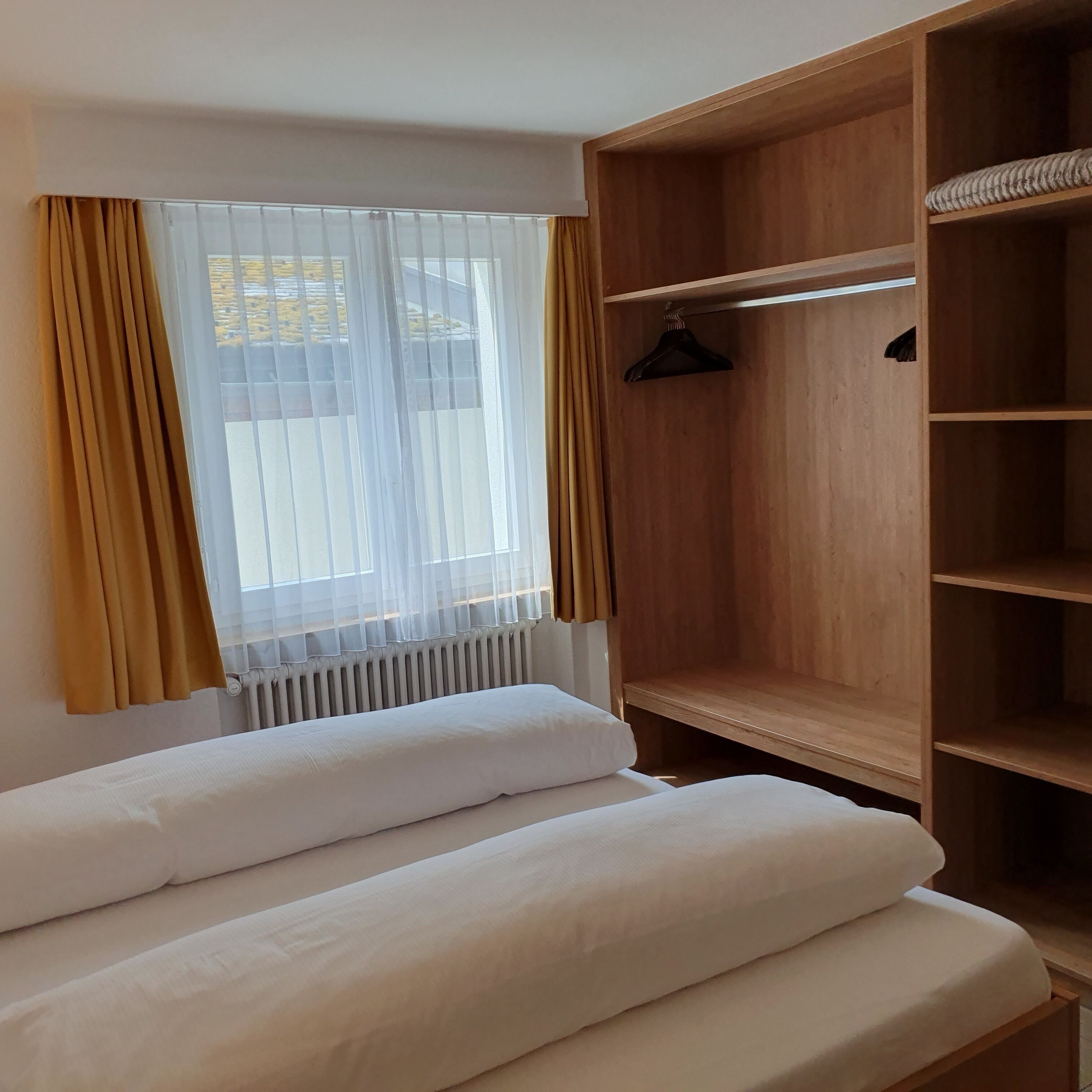Una habitación de hotel con una cama, un armario de madera y una ventana con cortinas.