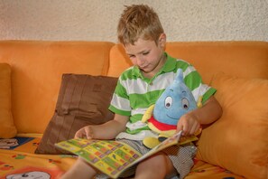 A child sitting on an orange couch with a book and a plush toy.
