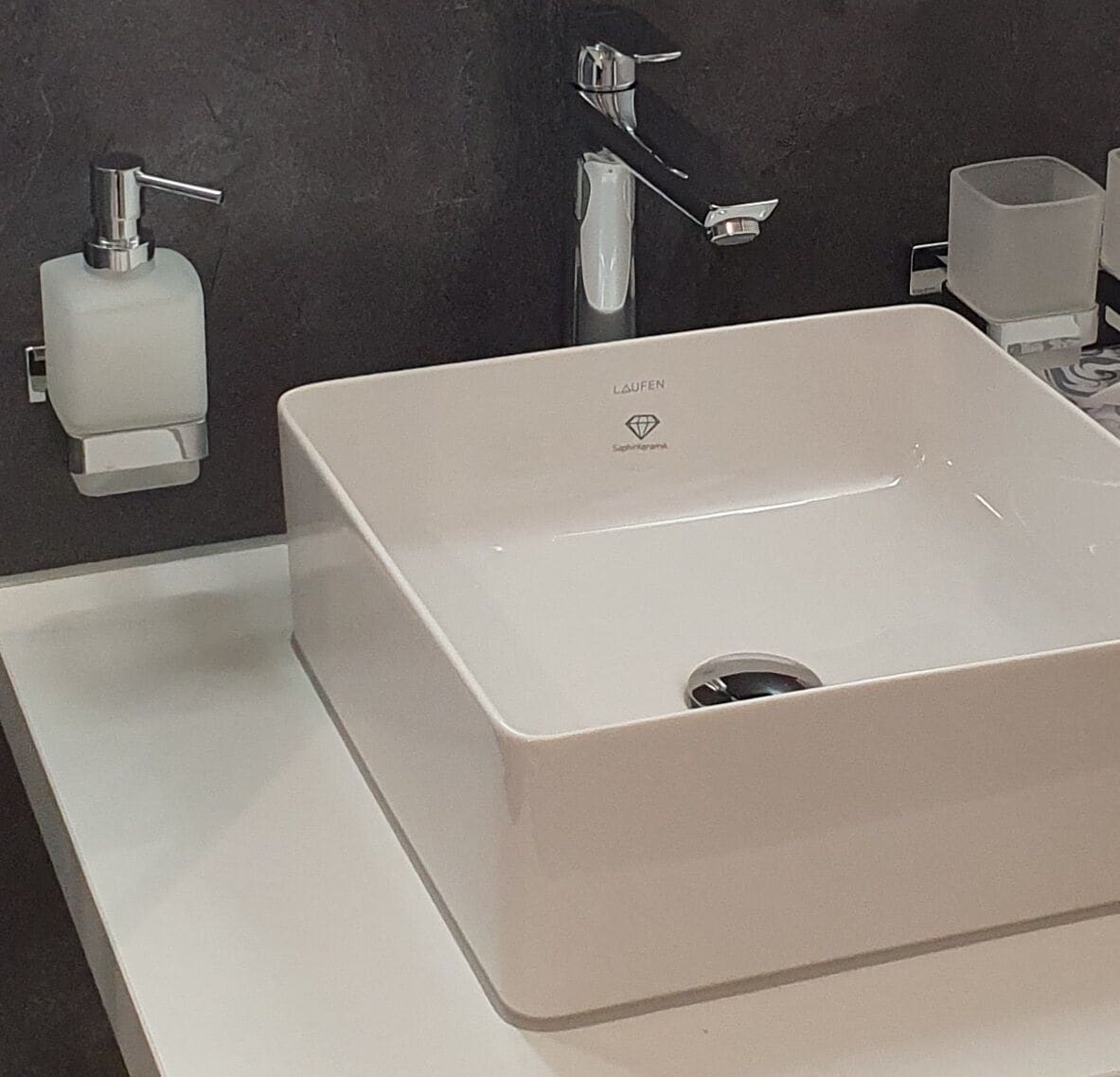 A modern bathroom with a white sink, chrome faucet, and a soap dispenser.