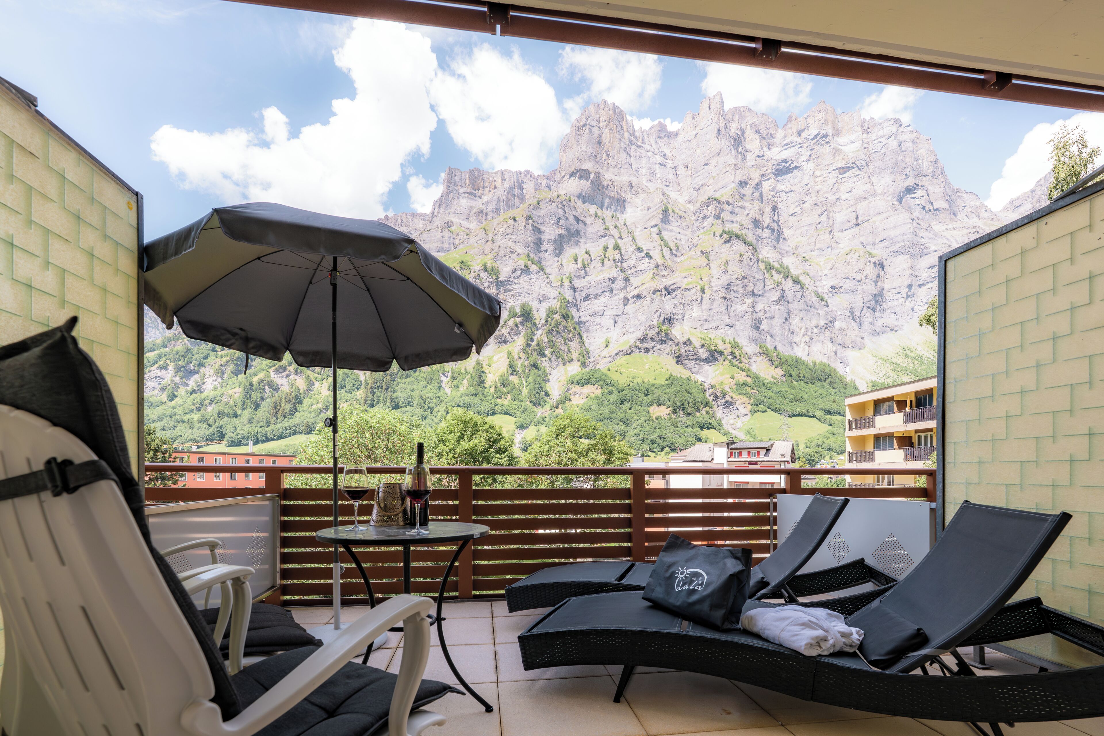 A balcony with outdoor furniture, a table with a bottle and glass, and a view of mountains.