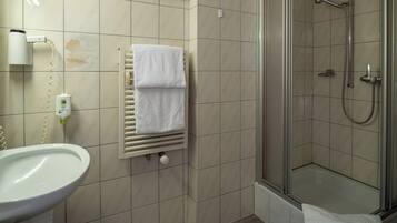 Un baño con lavamanos, toallero, ducha con puerta de cristal y retrete.