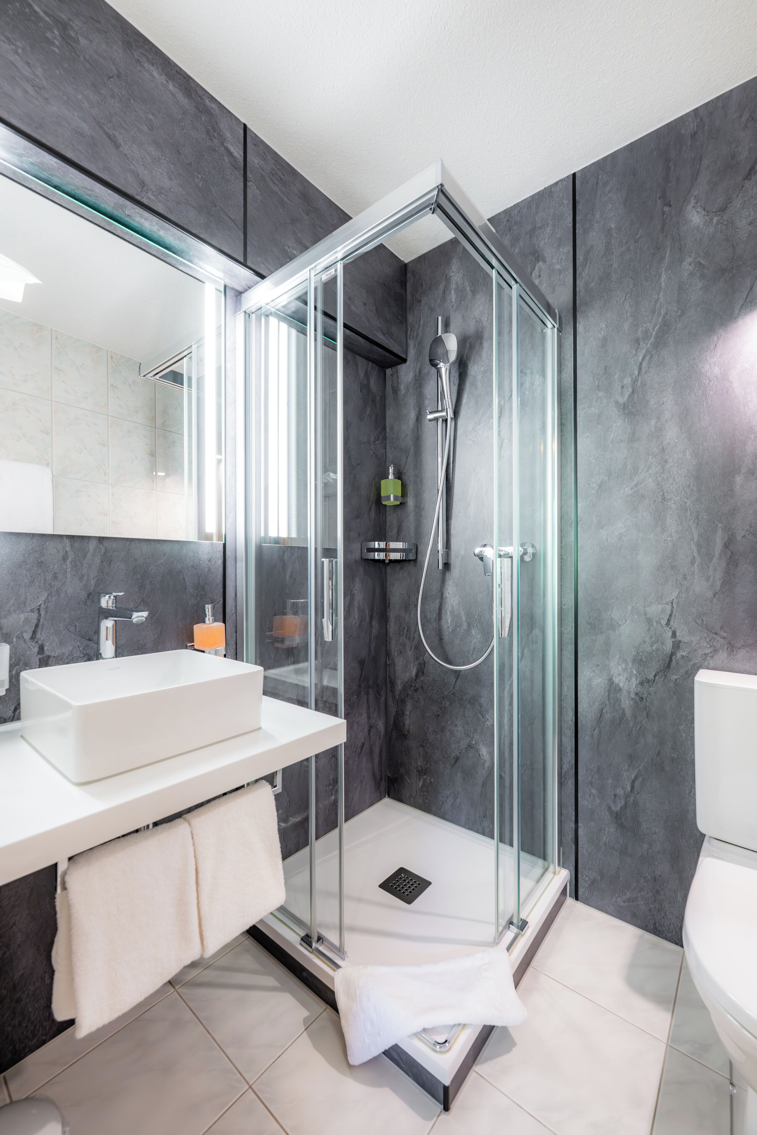 Un baño moderno con cabina de ducha de vidrio, un lavabo blanco y un espejo grande.