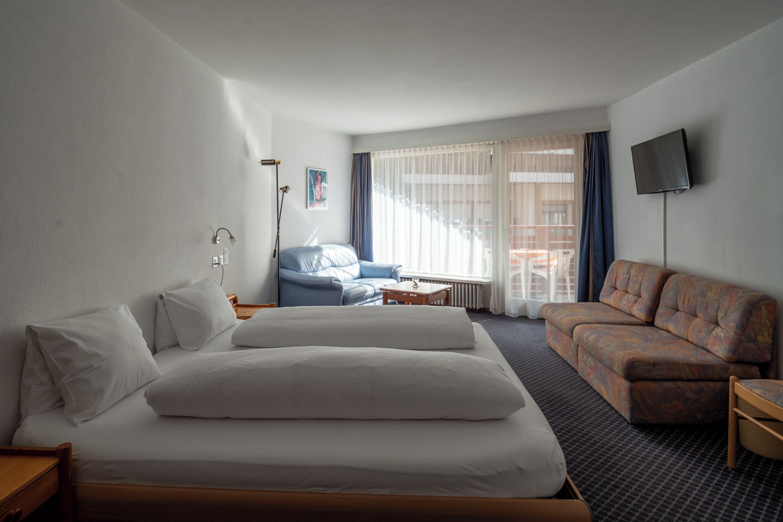 Ein Hotelzimmer mit einem großen Bett, einer Sitzecke, einem kleinen Tisch und einem an der Wand befestigten Fernseher.