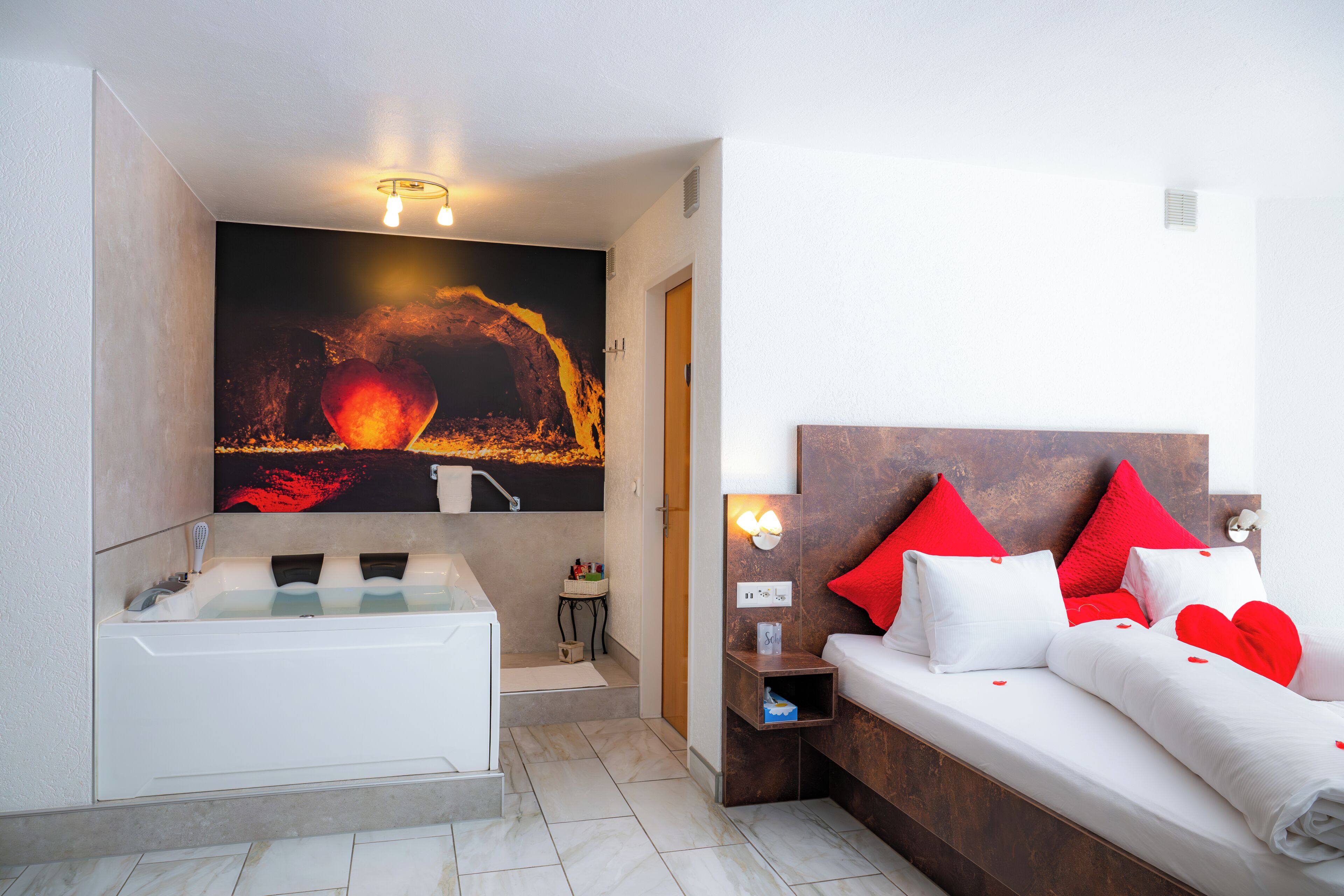 A modern hotel room with a large bed, a bathtub, and a wall-mounted artwork.