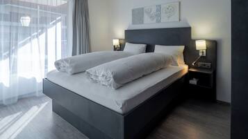 A modern hotel room with a large bed, two bedside tables with lamps, a window with curtains, and a wall with artwork.