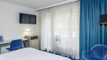 Una habitación de hotel con una cama, un escritorio con lámpara, un televisor y una silla.