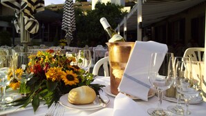 Una mesa dispuesta para una comida, con copas de vino, una botella de champán, un arreglo floral y un pastel.