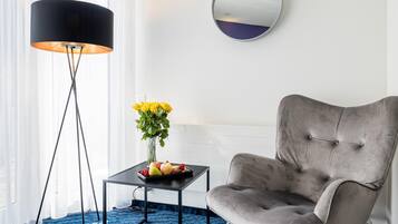 Una habitación con un sillón tapizado de color gris, una mesita negra con un jarrón de flores amarillas y una lámpara de pie.