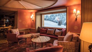 Um quarto aconchegante com sofá, poltronas, uma mesa redonda e uma janela com vista para uma montanha nevada.