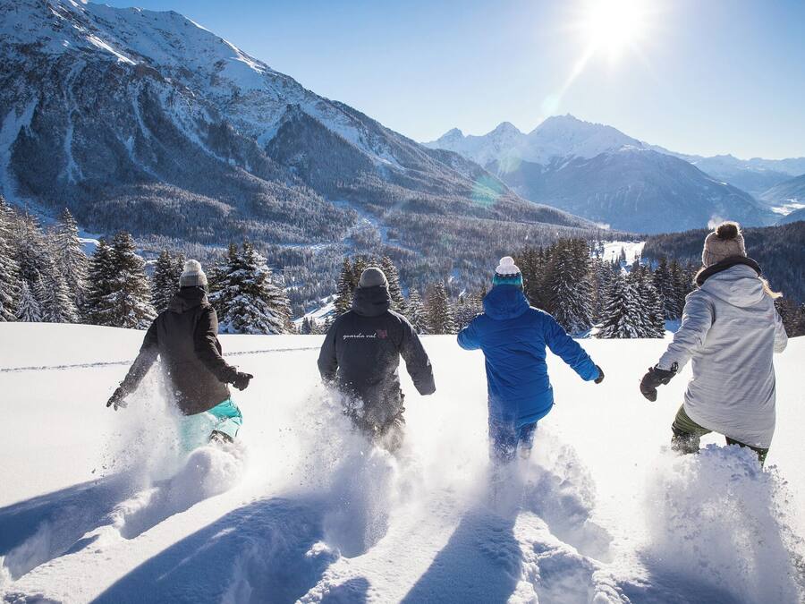 A group of people skiing down a snowy slope with a mountainous landscape in the background.