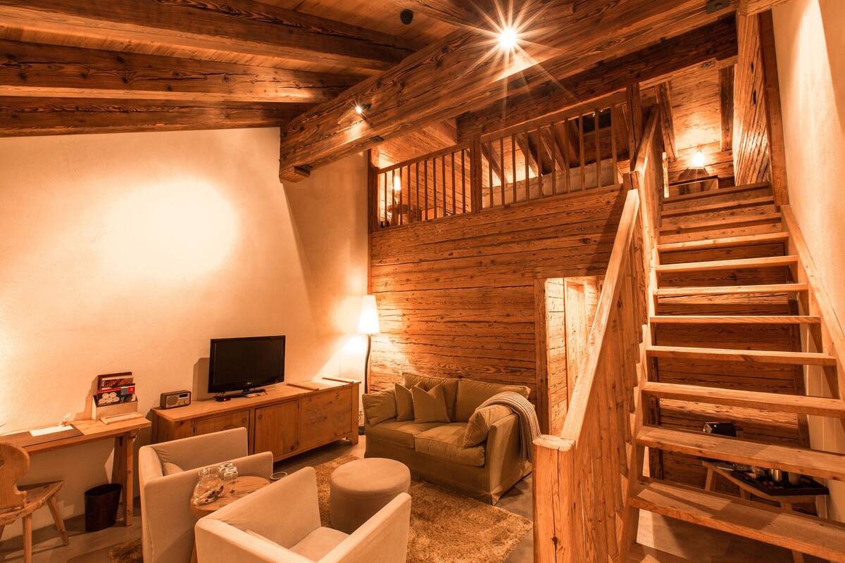 Una habitación acogedora con una escalera de madera, televisor, sofá y escritorio.