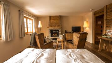 Ein gemütliches Zimmer mit Kamin, einem Bett, zwei Sesseln und einem Tisch mit Lampe.