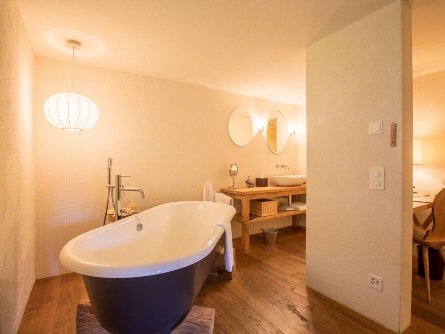 A modern bathroom with a freestanding bathtub, a wooden vanity, a mirror, and a light fixture.