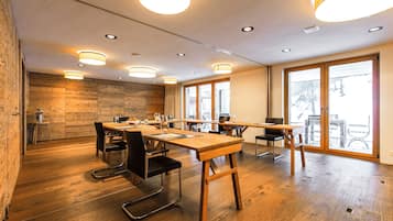 A spacious meeting room with wooden flooring, multiple tables, and chairs.