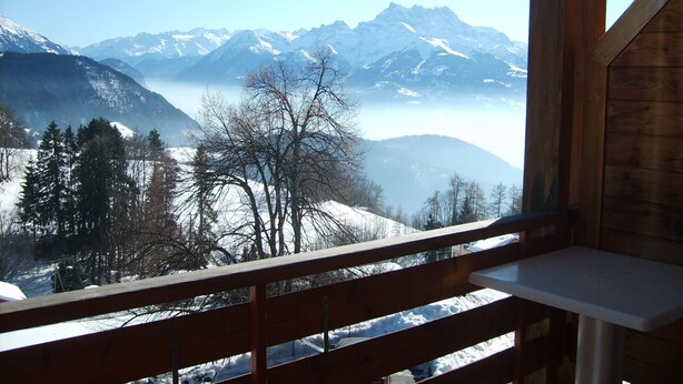 A wooden balcony with a view of snow-covered mountains and a clear sky. - Castel Club Leysin Parc Resort (Leysin)