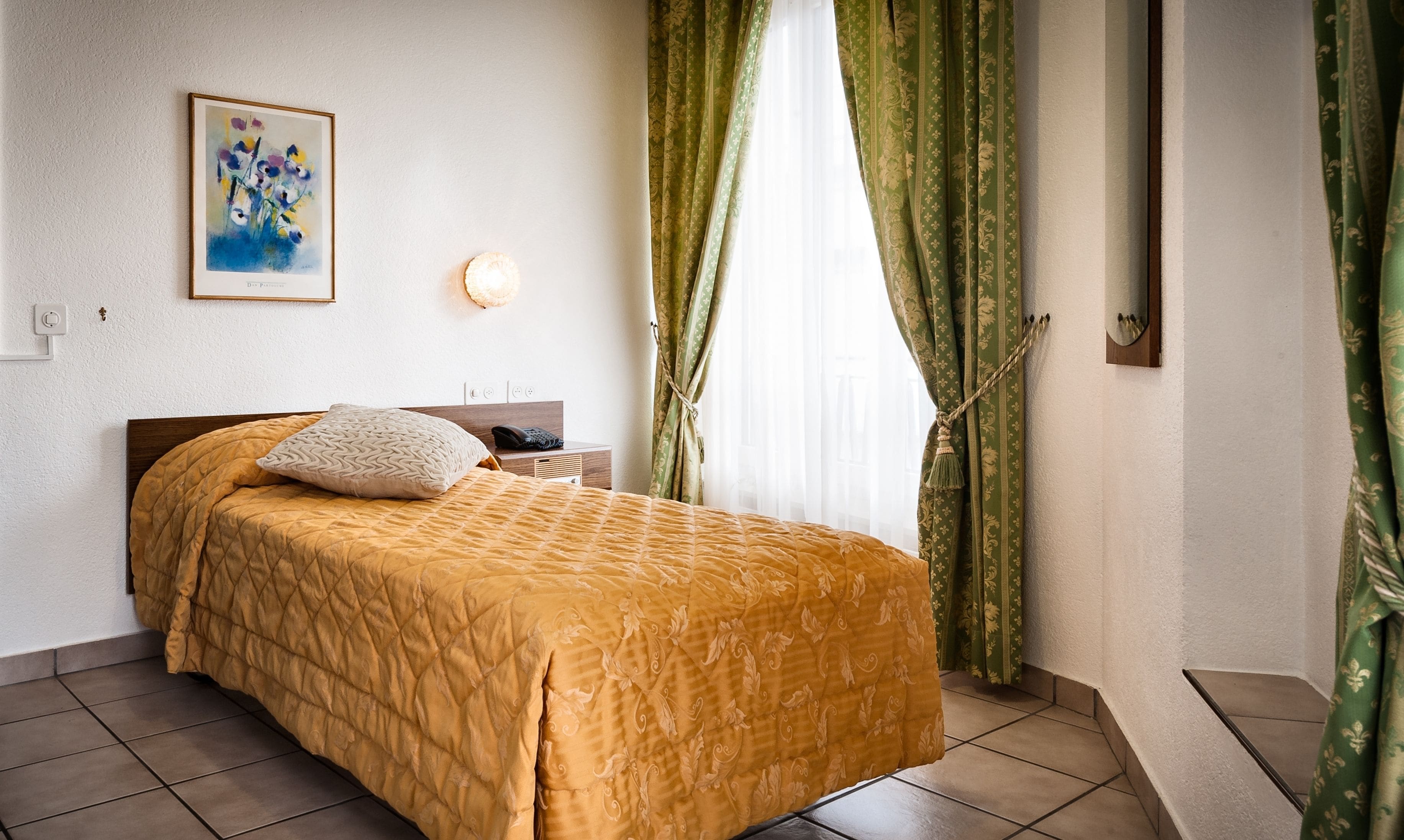 Un lit bien fait, recouvert d’une courtepointe, une table de chevet avec une lampe et un tableau accroché au mur.