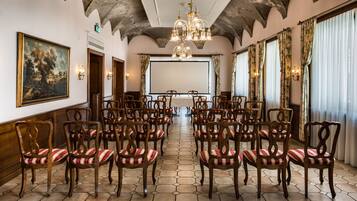 Une salle de conférence avec des chaises en bois, un grand tableau et un lustre.