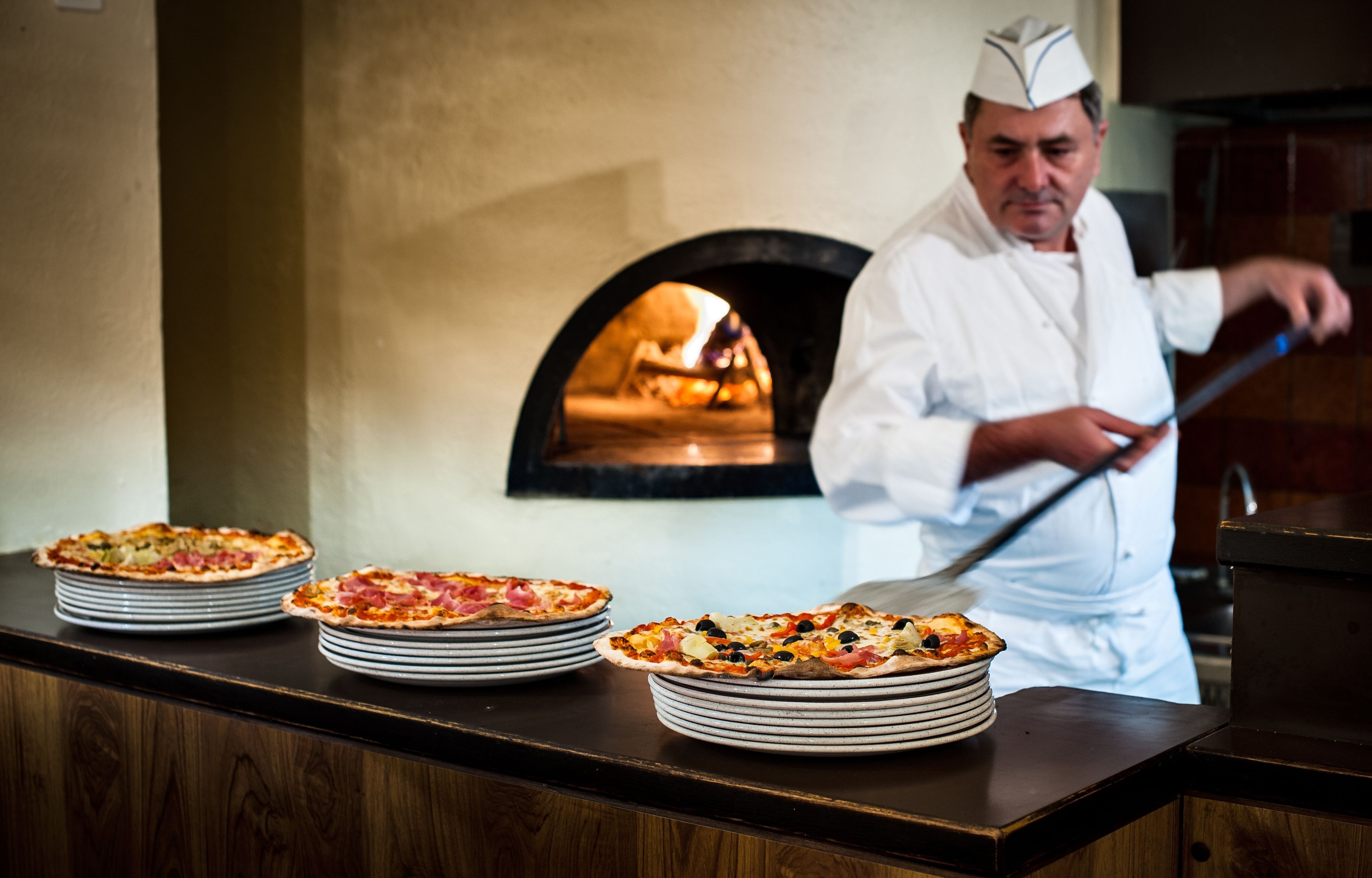 Ein Koch in weißer Uniform bereitet vor einem Holzofen Pizzen zu.