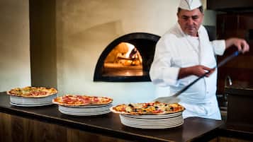 Ein Koch in weißer Uniform bereitet vor einem Holzofen Pizzen zu.
