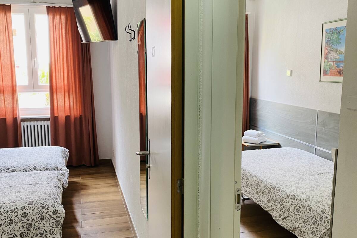 A hotel room with two beds, a TV mounted on the wall, and a window with curtains.