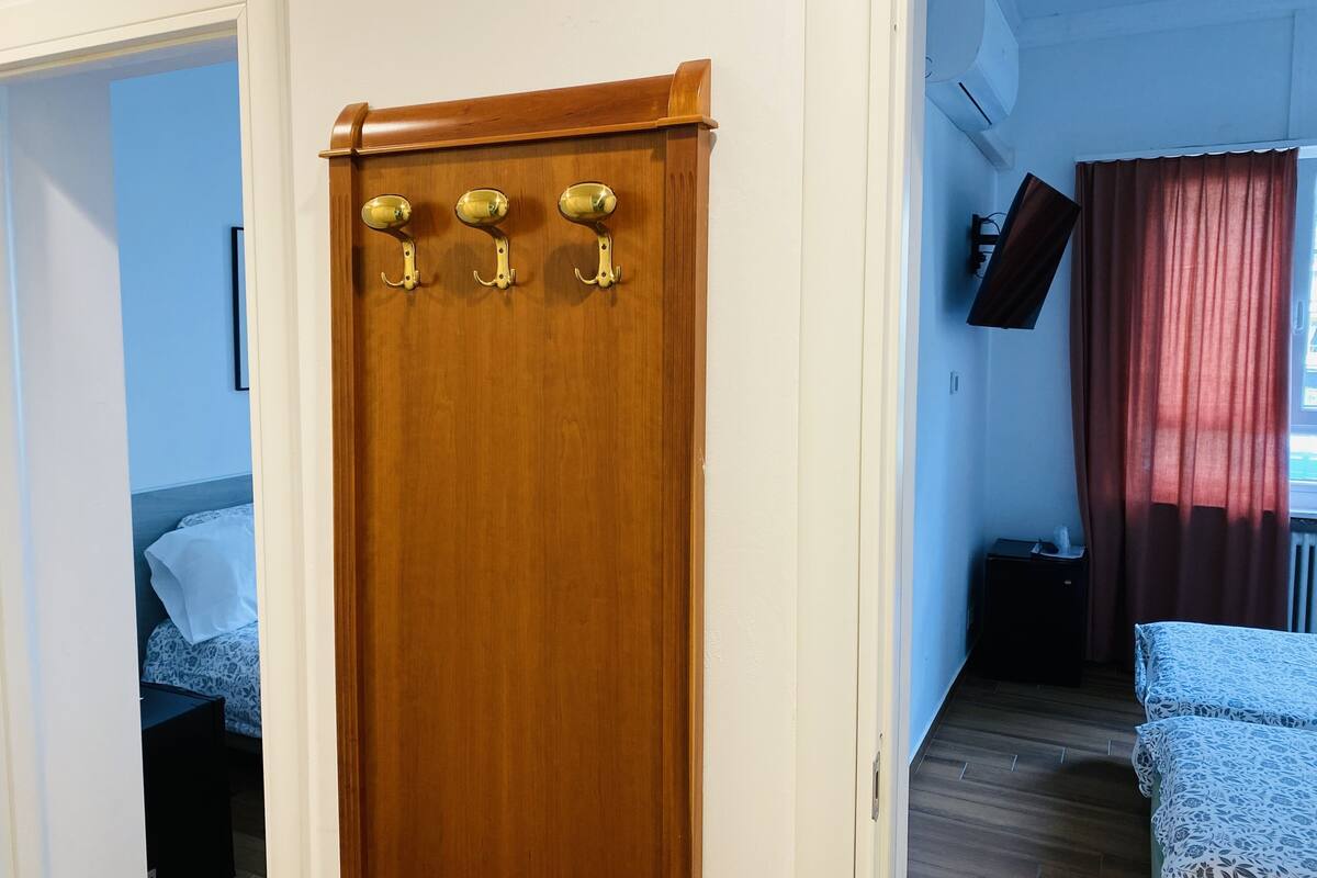 A wooden door with three brass handles, a bed with patterned bedding, and a television mounted on the wall.